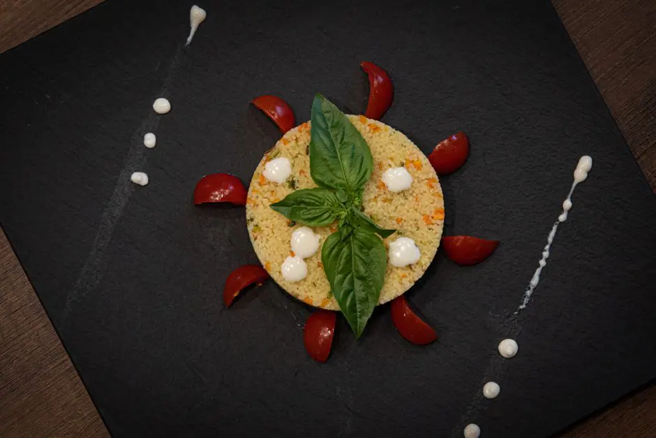 Couscous dish creatively plated with basil and cherry tomatoes on a slate plate.