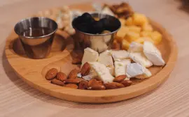 A close-up of a wooden tray featuring assorted cheeses, olives, nuts, and honey.