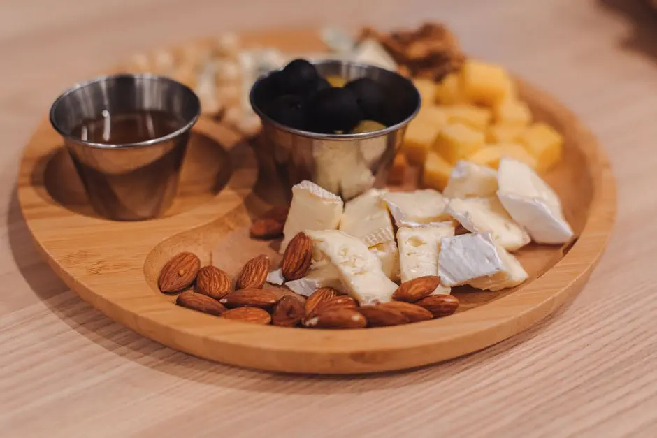 A close-up of a wooden tray featuring assorted cheeses, olives, nuts, and honey.